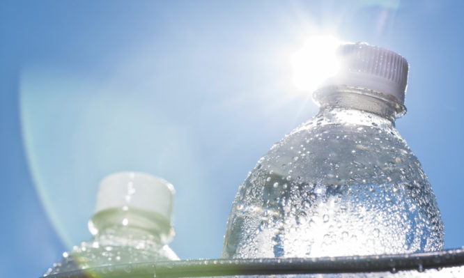 A close-up of a plastic water bottle in a bucket of ice as the Sun shines down on a hot Summer day. It is a good idea to keep hydrated while doing activities on a hot day.