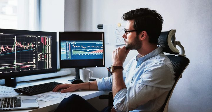 Busy working day. Side view of successful trader or businessman in formal wear and eyeglasses working with charts and market reports on computer screens in his modern office